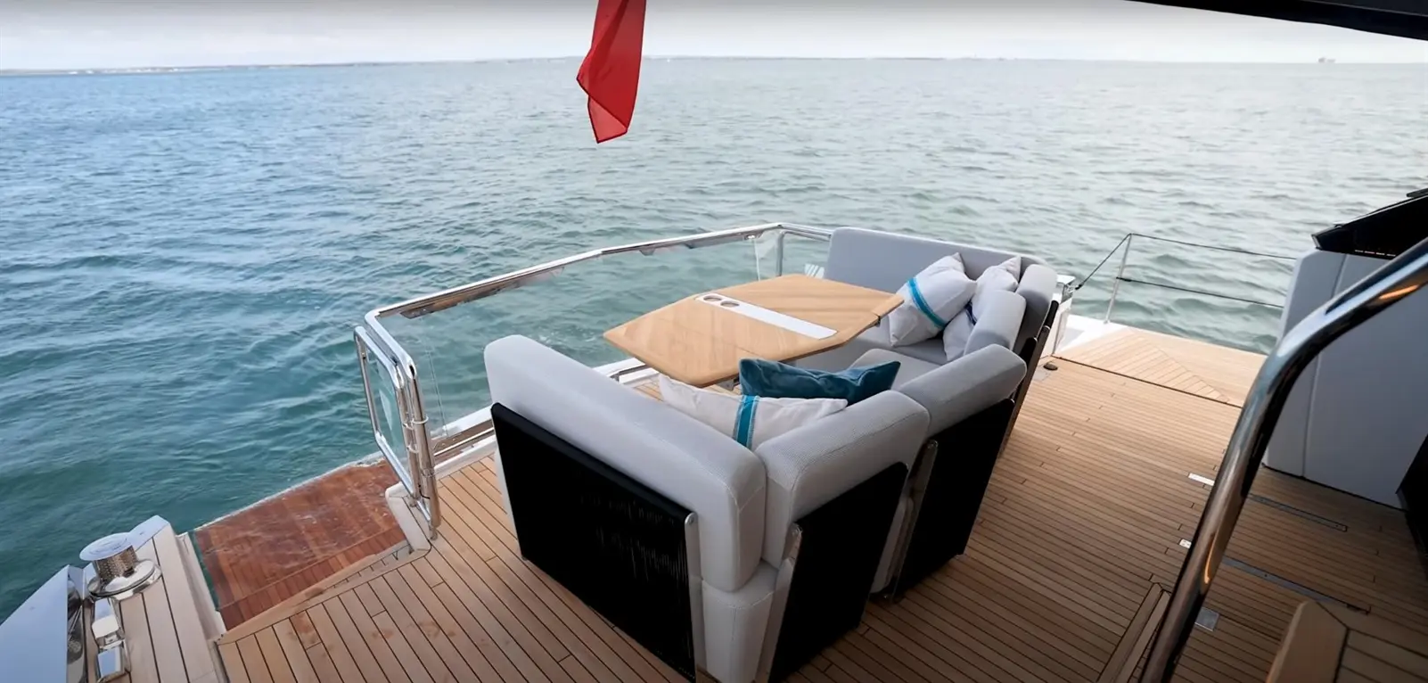 Luxury yacht deck featuring a modern seating area with cushions, a wooden table, and a scenic ocean view.